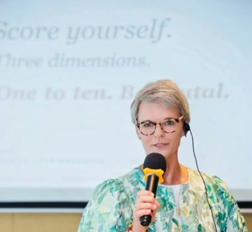 Ivanka Menken speaking in front of a slide that reads: score yourself, one to ten