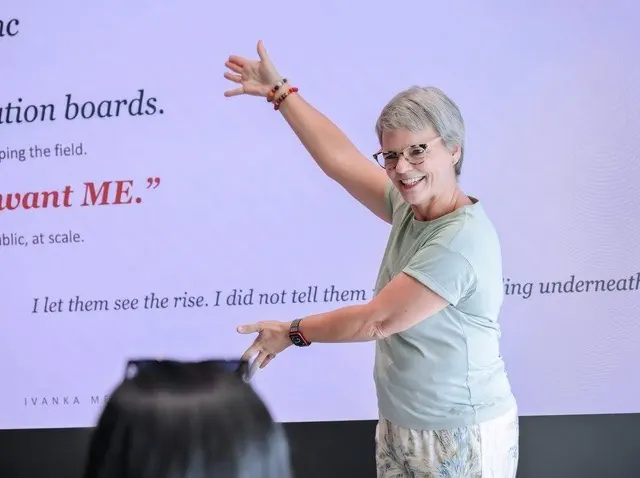 Ivanka Menken presenting, pointing to the slide behind her